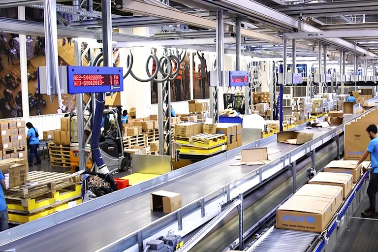 People working in a warehouse where boxes roll along a conveyor belt.