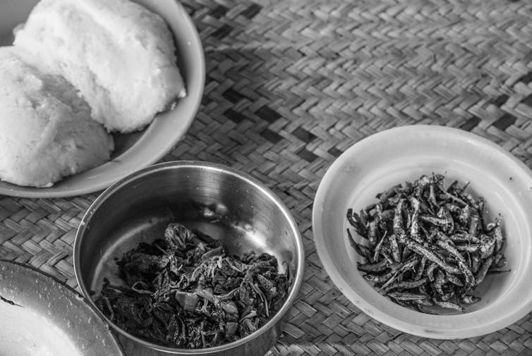 Three dishes of food in different metal plates rest on a woven mat.