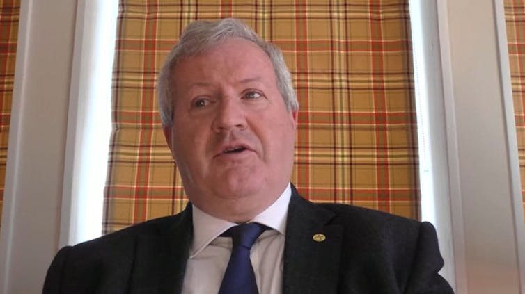 SNP MP Ian Blackford sits in front of his tartan curtain.