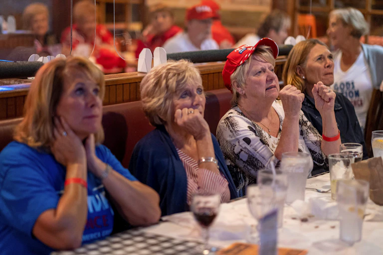 Four women sitting at a table watch the presidential election returns.