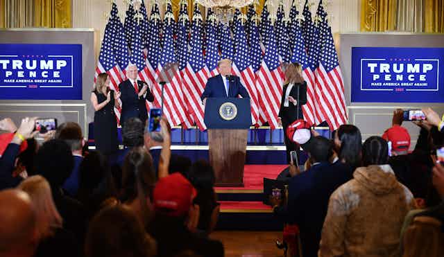 Trump flanked by his wife and vice president speaks in front of an array of American flags at the White House