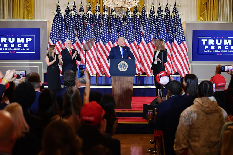 Trump flanked by his wife and vice president speaks in front of an array of American flags at the White House