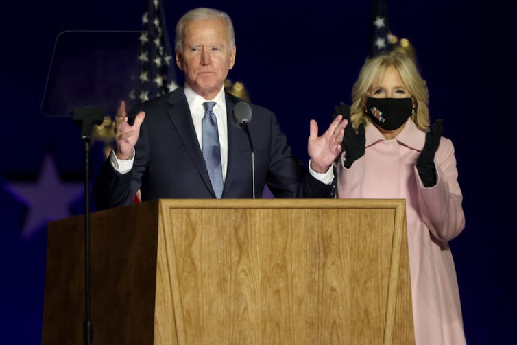 Biden speaking at a lectern next to his wife, who wears a face mask