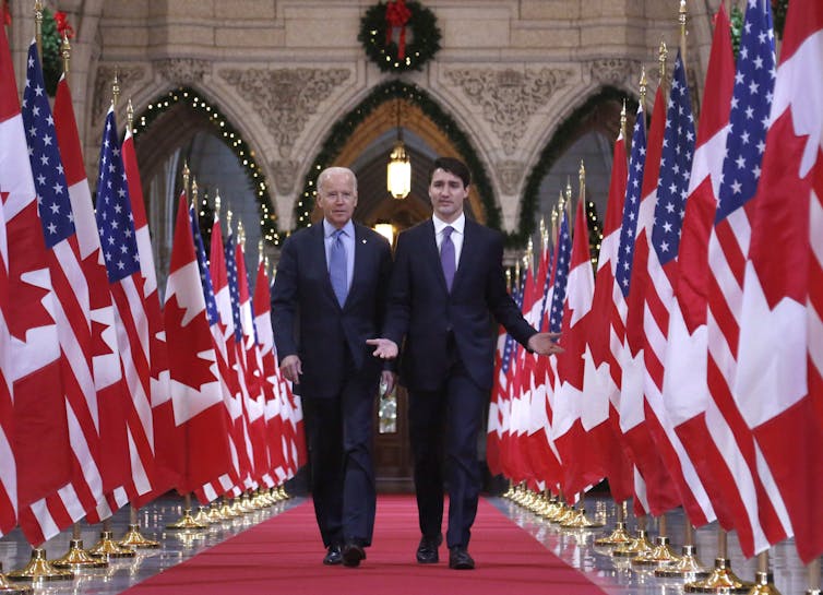 Joe Biden and Justin Trudeau walk down the Hall of Honour on Parliament Hill in Ottawa, flanked by Canadian and American flags.