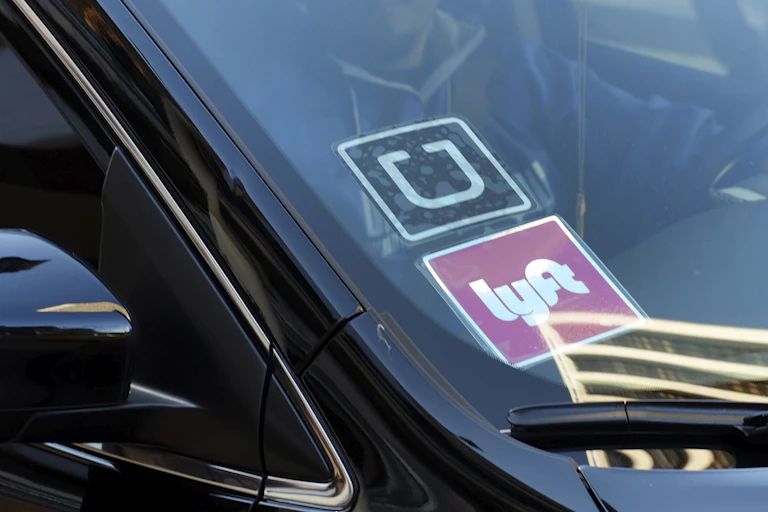 A ride-share car displays Lyft and Uber stickers on its front windshield in downtown Los Angeles.