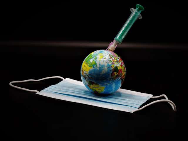 Illustration of a globe injected by a syringe, resting on a face mask.