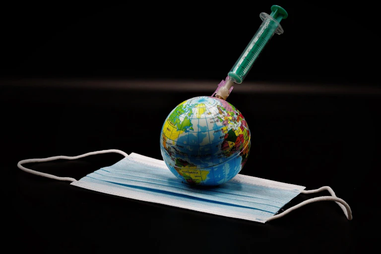 Illustration of a globe injected by a syringe, resting on a face mask.