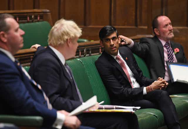 Rishin Sunak and Boris Johnson lean across a social distance to talk in parliament. 
