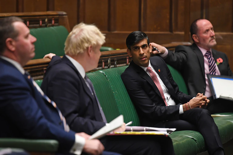 Rishin Sunak and Boris Johnson lean across a social distance to talk in parliament.