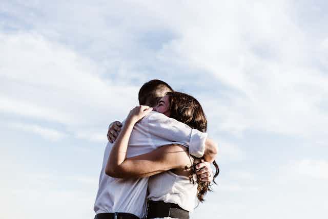 A young man and woman hugging outdoors.