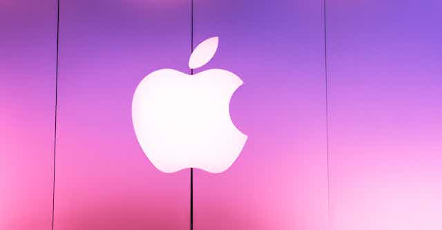 The Apple corporate sign outside a store lit up in pink.