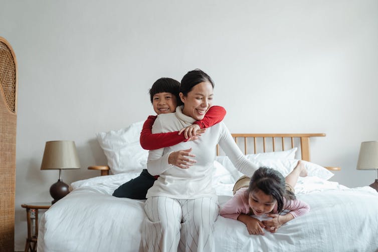 Cheerful mother playing with and hugging her children on the bed.