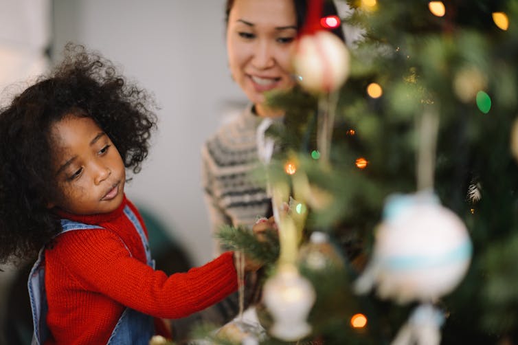 Child and mother decorate Christmas tree.