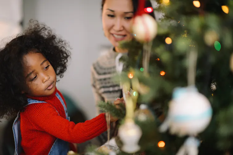 Child and mother decorate Christmas tree.