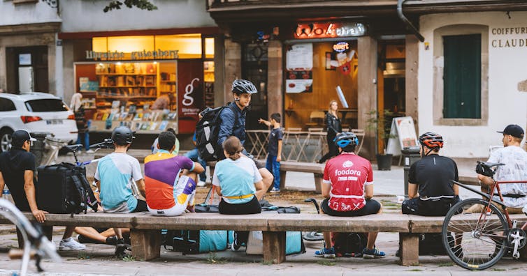 Delivery men sitting sideways next to their waiting bikes.