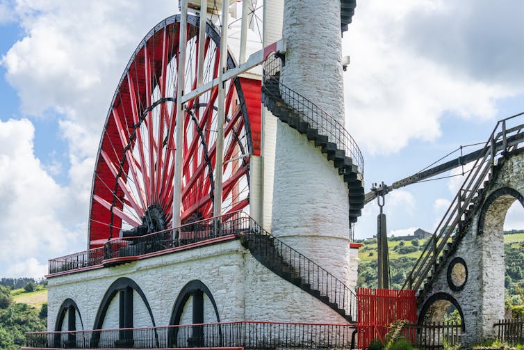 A large red and white wheel next to a tower.