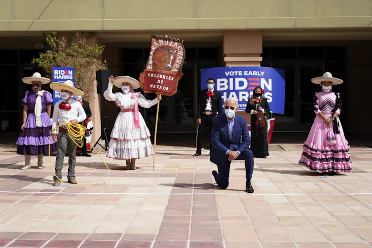 Joe Biden takes a knee in front of five performers in costume