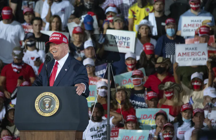 Donald Trump in front of a podium with supporters behind.