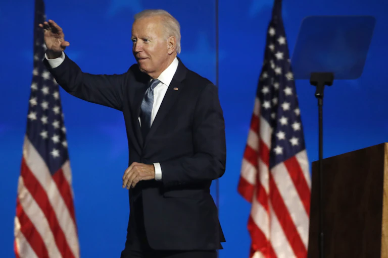 Joe Biden on stage with two American flags behind him.