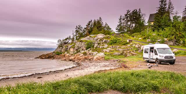 A white van sits near a beach.