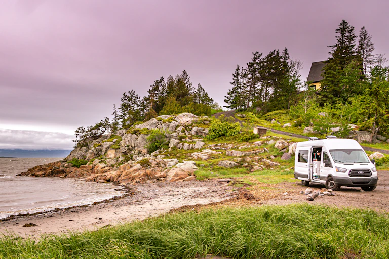 A white van sits near a beach.