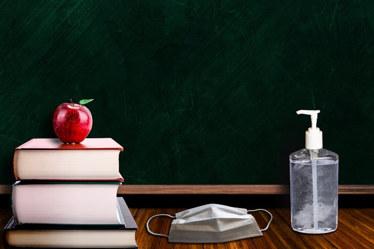 Textbooks, a mask and sanitiser on a teacher's desk.