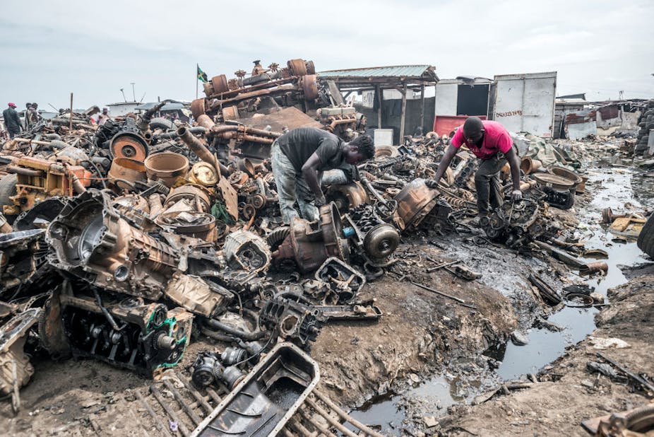 Two men sort through heap of discarded metal items next to a ditch 