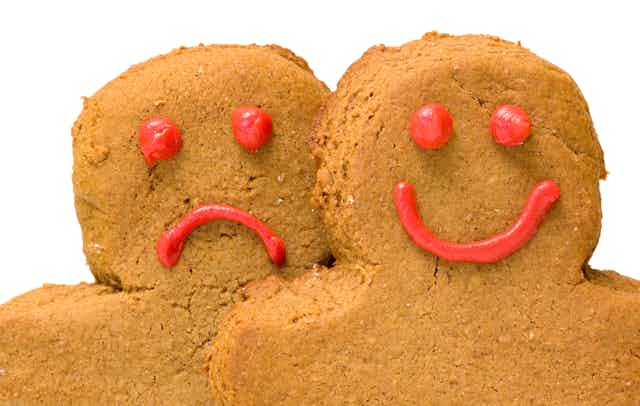 Two people-shaped cookies, one with a smiley face, one with a frown.