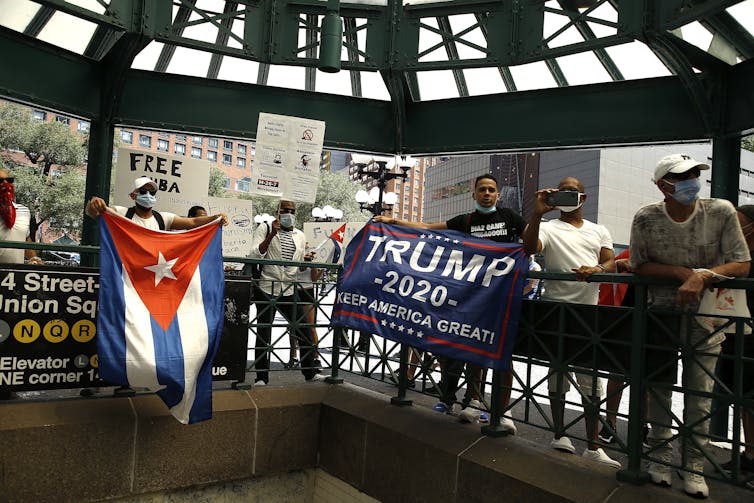 People in face masks hold Cuban flags, pro-Trump signs and 'free Cuba' signs outside a subway station