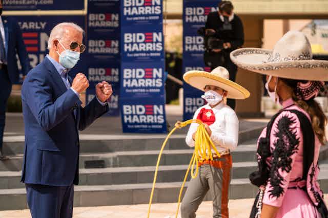 Biden wears a face mask and interacts with children in traditional Mexican wear
