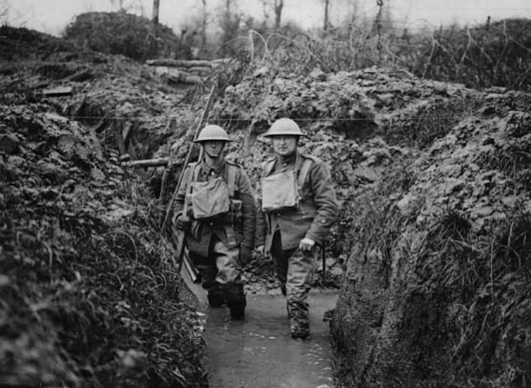 Two World War I soldiers up to their knees in muddy trench water.