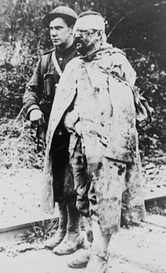 A World War I soldier helping an injured comrade with a head wound.