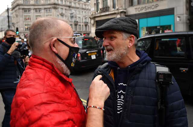 A man wearing a mask argues with a man not wearing a mask 