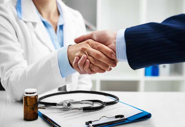 Cropped photo of a female doctor shaking hands with someone in a pinstriped suit.