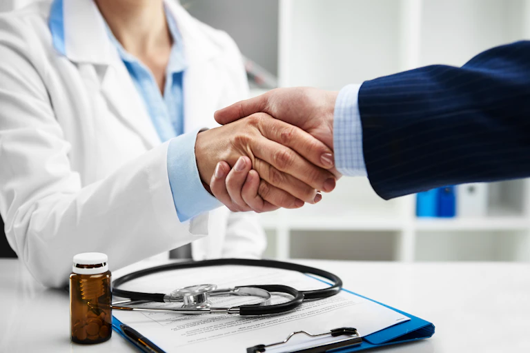 Cropped photo of a female doctor shaking hands with someone in a pinstriped suit.
