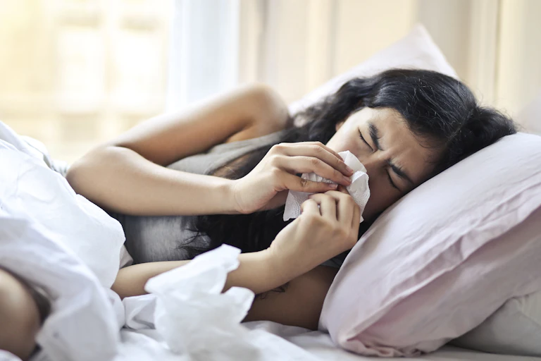 An ill woman in bed, blowing her nose.