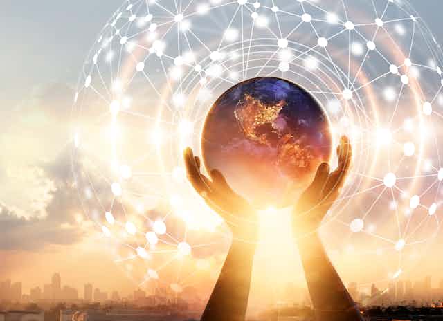A pair of hands holding a globe of the Earth in front of a sunrise, with an abstract network diagram superimposed.