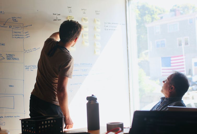 young man presents at whiteboard to a colleague