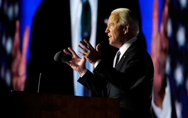 President-elect Joe Biden speaks as he is seen on the large monitor behind him on Nov. 7, 2020, in Wilmington, Del.