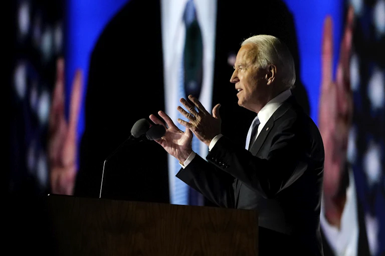 President-elect Joe Biden speaks as he is seen on the large monitor behind him on Nov. 7, 2020, in Wilmington, Del.