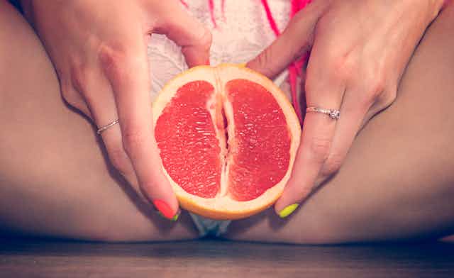 woman holding grapefruit in front of crotch.
