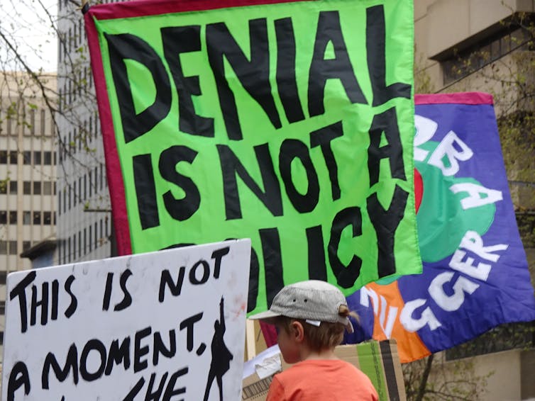 A protest sign saying 'Denial is not a policy'.