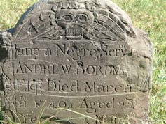 An old grave marker sits in a grassy burial ground