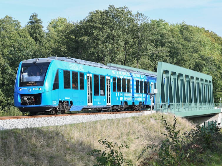 A blue train passes over a green bridge.