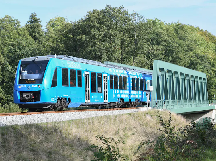 A blue train passes over a green bridge.