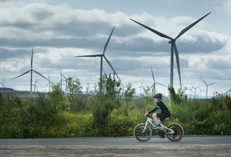 Wind turbines turn on a bright day with a child cycling in the foreground.