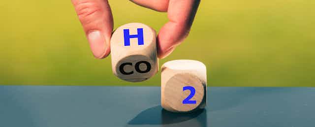 A hand holding a dice with "H" prepares to place it next to one reading "2".