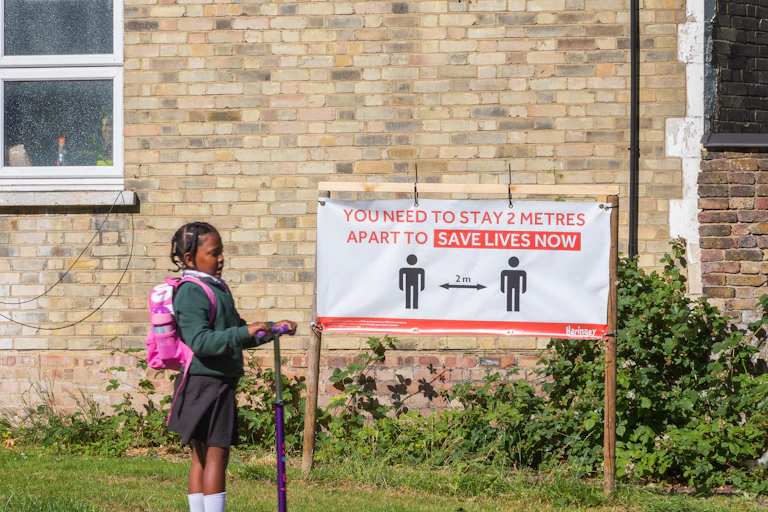 Girl on scooter by social distancing instruction sign