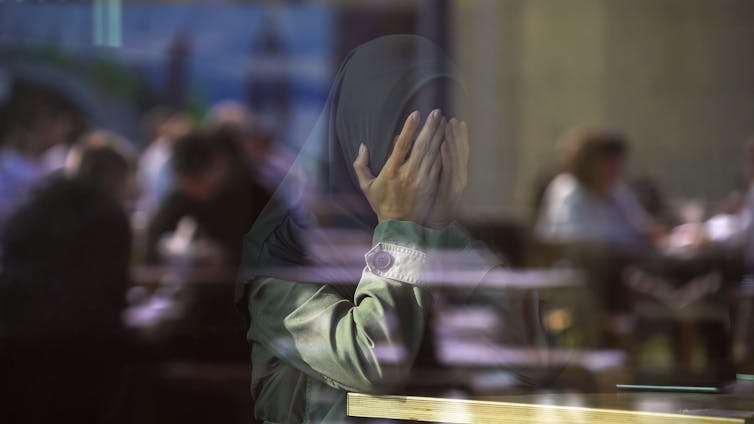Desperate Muslim female crying in cafe, covering face with hands
