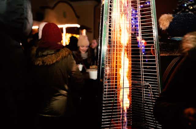 An outdoor heater with people socialising in background.